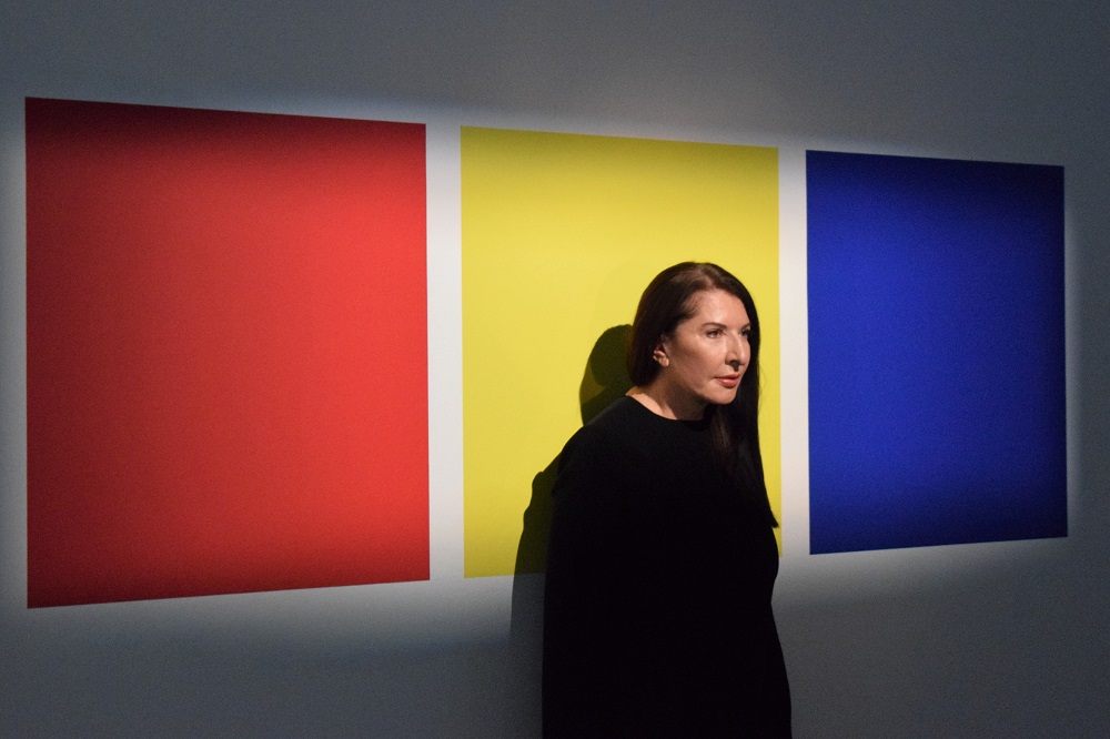 Marina Abramovic steht vor Farbfeldern in Rot-Gelb-Blau.