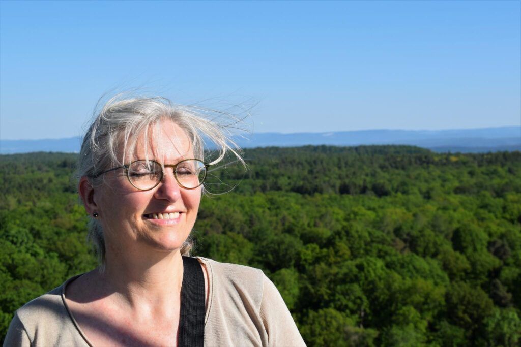 Eine Frau mit geschlossenen Augen steht vor einer Waldlandschaft