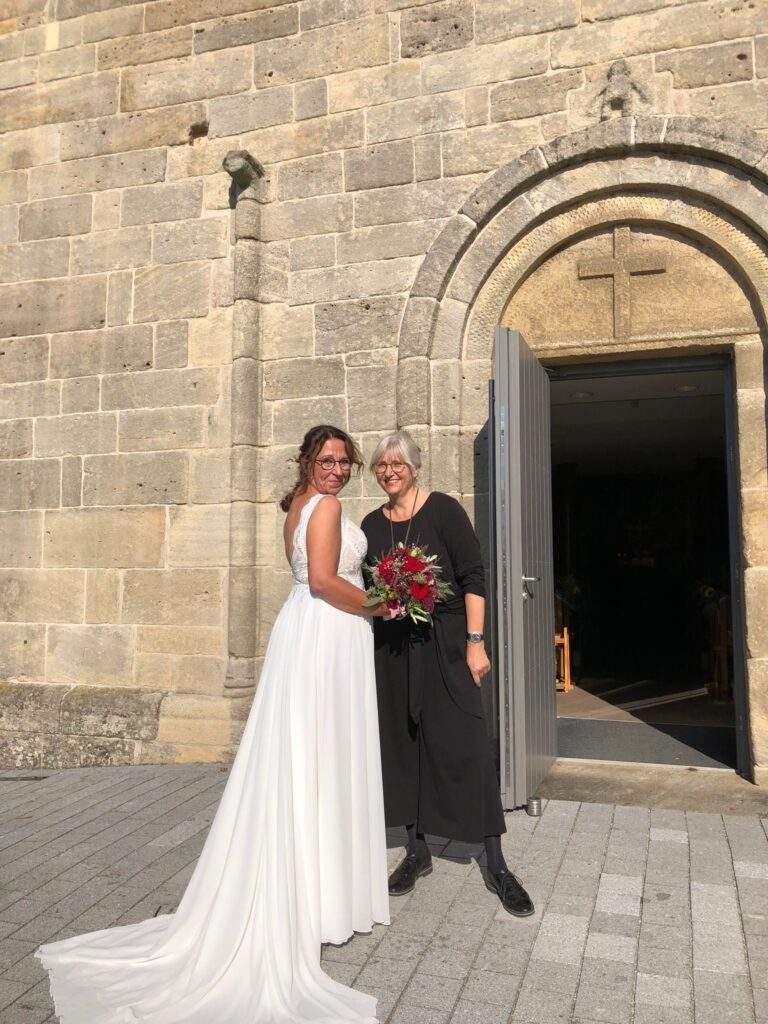 Frau Bachmann mit einer Braut vor einer Kirche