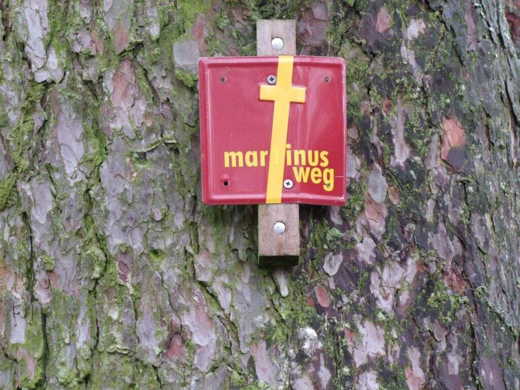 Eine rote Wegmarke mit einem gelben Kreuz an einem Baum
