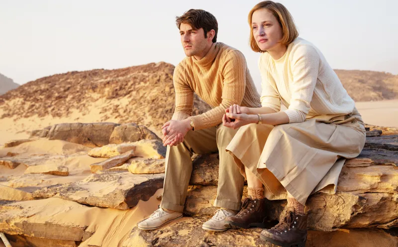 Filmstill aus dem Film "INgeborg Bachmann - Reise in die Wüste"_ein Mann und eine Frau sitzen in iener ockerfarbenen Wüstenlandschaft